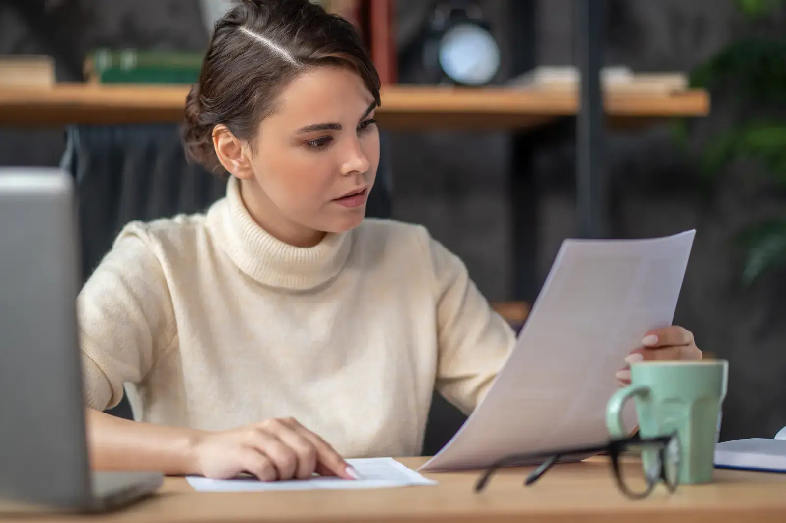 A woman at a desk reading a printed document closely